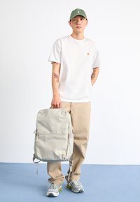 Pelēks auduma mugursoma ar divām sānu kabatām, ar rāvējslēdzēju slēgtu priekšējo nodalījumu un regulējamām siksnām. Logo priekšpusē, gluda tekstūra.