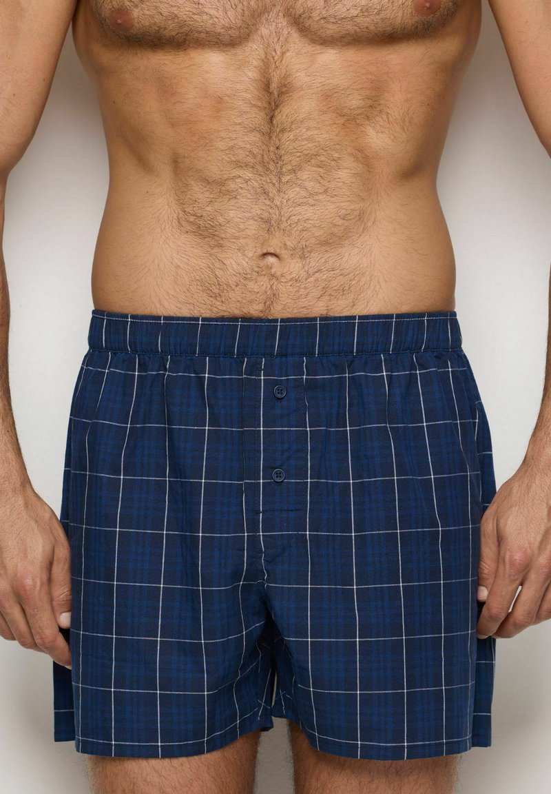 Marineblauwe geruite boxershorts met een zachte textuur, voorzien van een comfortabele elastische tailleband en twee voorste knopen. Een witte rasterpatroon accentueert het ontwerp.