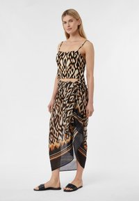 Schwarzes und beiges gemustertes Crop-Top mit dünnen Trägern, kombiniert mit einem passenden Wickelrock. Der Stoff ist leicht und fließt frei.