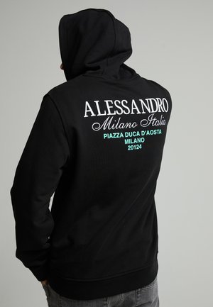Person trägt einen schwarzen Kapuzenpullover mit weißem und türkisfarbenem Text, der auf Alessandro Milano, Italien und Piazza Duca D'Aosta auf der Rückseite verweist.