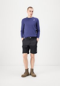 Paarse lange mouwen shirt, zwarte cargoshorts met zakken en lichtbruine veterschoenen. Eenvoudig ontwerp met een casual pasvorm.