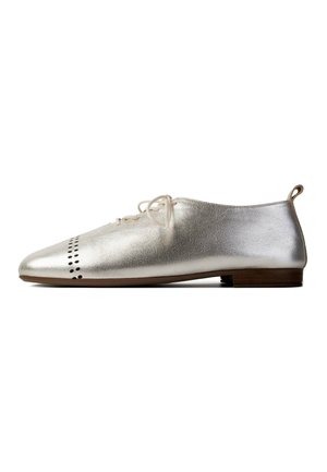 Zilverkleurige metallic oxford schoen met lage hak, vooraan voorzien van een geperforeerd patroon, crèmekleurige veters en een kleine bruine hak tegen een witte achtergrond.