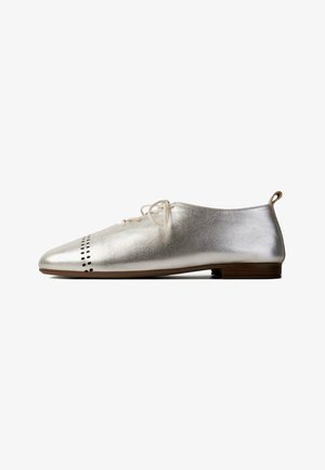 Silver metallic low-heeled oxford shoe with front perforated pattern, cream laces, and a small brown heel against white background.