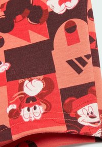 Tela de algodón con una paleta de colores en rojo brillante y tonos oscuros, adornada con patrones de Mickey Mouse, formas geométricas y detalles de costura texturizada.