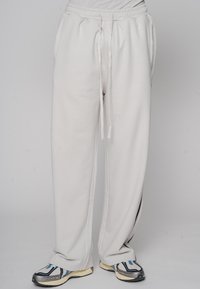 Hellgraue Jogginghose mit elastischem Bund und verstellbarem Kordelzug, Vordertaschen und seitlichem schwarzen Streifendetail. Kombiniert mit stylischen Sneakers.