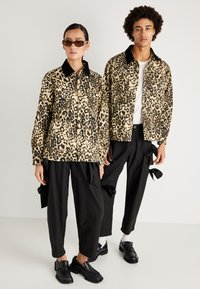 Leopárd mintás dzsekik barnás-fekete színkombinációban, gallérral és gombos záródással, laza fekete nadrágokkal párosítva.