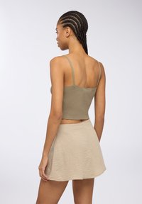 Top crop a coste verde oliva con spalline sottili abbinato a una gonna svasata beige chiaro, caratterizzata da un tessuto strutturato e chiusura con zip sul retro.