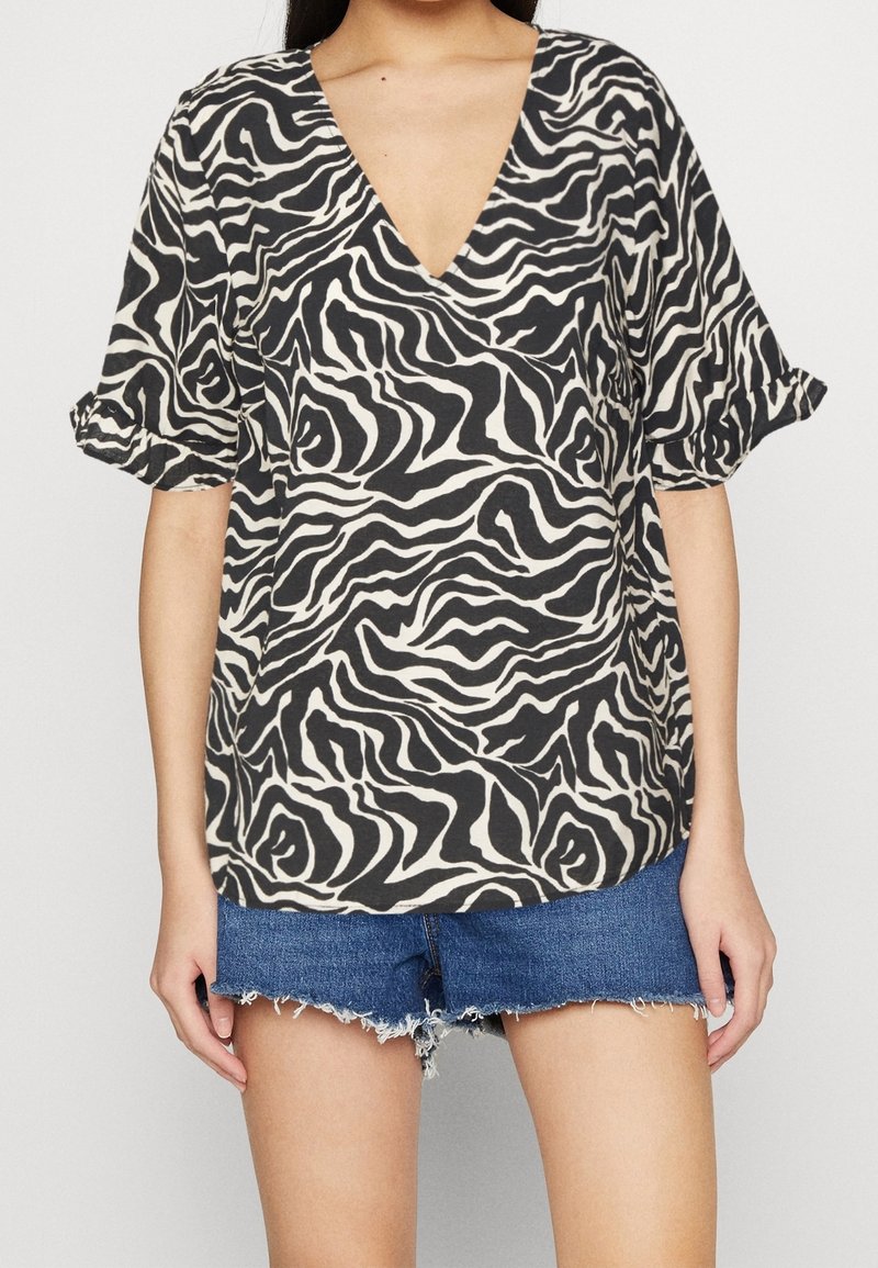 Femme portant un chemisier imprimé zèbre noir et blanc avec des manches bouffantes et un short en denim bleu coupé.