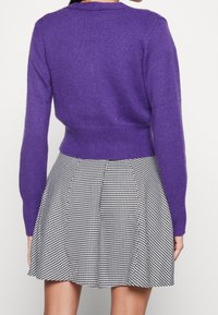 Lila gestrickter Pullover mit taillierter Passform, kombiniert mit einem schwarz-weißen Hahnentrittmuster-Rock mit Falten. Weicher Stoff, lässiges Design.