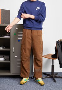 Sudadera azul marino con logo blanco de Nike, pantalones cargo marrones y zapatillas multicolores. Diseño simple, ajuste casual y tela texturizada.
