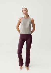 Top senza maniche grigio chiaro con dettagli delle cuciture e scollo rotondo, abbinato a leggings svasati color bordeaux realizzati in tessuto liscio.