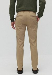 Beiga chinos med slim fit, som har två bakfickor med dragkedja, kombinerade med en grön tröja. Slät tyg och skräddarsydd design.