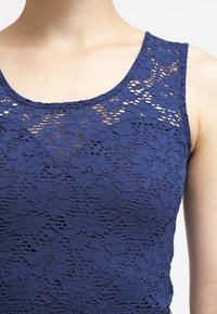 Granatowy top na ramiączkach z koronką, z kwiatowym wzorem i okrągłym dekoltem, o teksturowanym wykończeniu i widocznymi detalami szwów.