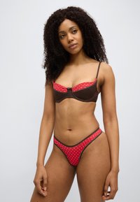 Κόκκινο σουτιέν με πουά και αντίστοιχο στρινγκ με καφέ λεπτομέρειες, με δομημένο σχεδιασμό και ρυθμιζόμενους ιμάντες. Ομαλή υφή.