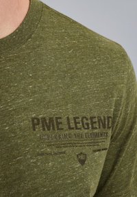 Olivgrünes T-Shirt aus strukturiertem Stoff, mit einem dunklen Druck vorne, auf dem "PME LEGEND" und das Logo "EXPLORING THE ELEMENTS" zu sehen sind.