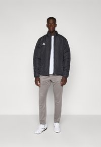 Svart puffer-jakke med quiltet tekstur og stående krage, kombinert med lysegrå bukser og hvite sportssko.