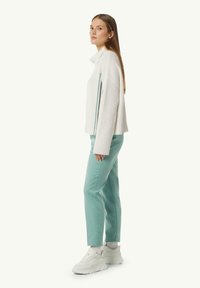 Strukturierter weißer Pullover mit hohem Kragen, kombiniert mit mintgrünen Hosen und weißen Sneakern. Enthält kontrastierende Seitendetails.
