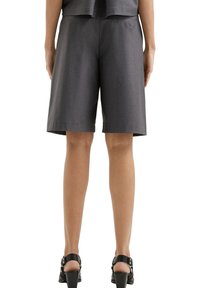 Donkergrijze op maat gemaakte shorts met een gladde textuur, tot de knie, met een platte tailleband en zijzakken, gecombineerd met zwarte haksandalen.
