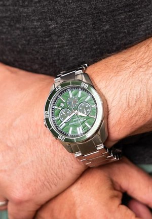 Orologio da uomo con bracciale in acciaio inossidabile, quadrante verde con texture, indici delle ore argentati e tre sottodial. La cassa è rotonda e metallica.