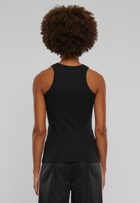 Černé bavlněné tílko s přiléhavým střihem, širokými ramínky a kulatým výstřihem, s hladkou texturou a bez viditelných ozdob.