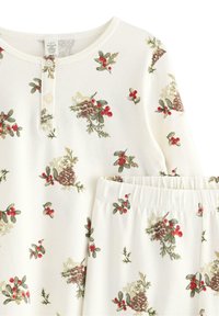 Ensemble de pyjama en coton blanc présentant un motif floral de cônes de pin, de houx et de baies rouges, avec un détail de bouton sur le haut et une taille élastique sur le pantalon.