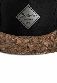 Cappello nero con visiera in sughero, dotato di un patch in gomma a forma di diamante con la scritta "Blackskio Premium Supplies Co." in lettere argentate.