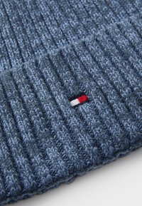 Gorro de punto azul con textura acanalada. Presenta un pequeño logotipo bordado en colores rojo, blanco y azul en el puño.