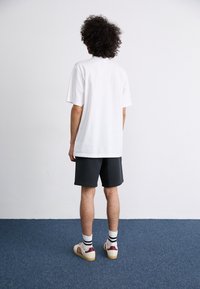 White short-sleeve t-shirt, gray shorts, beige sneakers with burgundy stripes, and white socks with black lines. Plain background.