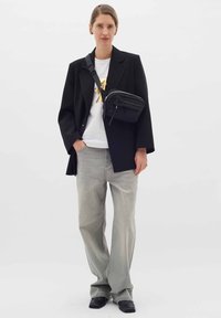 Črn oversize blazer preko bele majice z metalnim dizajnom, v kombinaciji s svetlo sivo širokima hlačami in črno torbico čez rame.