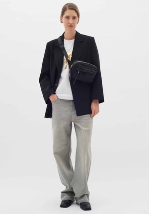 Sort oversized blazer over en hvid t-shirt med metallisk design, parret med lysegrå vide bukser og en sort crossbody taske.