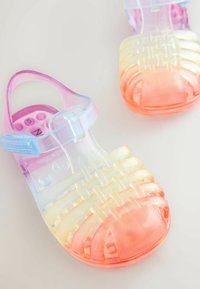 Permatomi želė sandalai su ombre dizainu nuo rožinės iki oranžinės spalvos. Viršus su dirželiais ir sagtimi; tekstūruotos rožinės pado dalys.