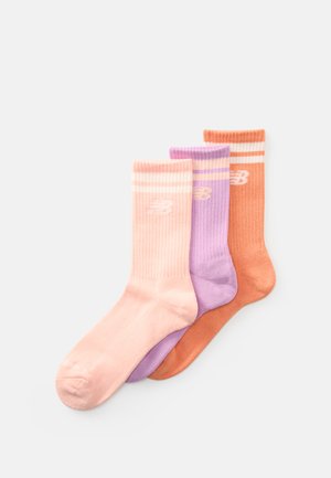 Trois paires de chaussettes en côtes pliées de couleur rose pastel, lavande et orange avec des rayures blanches et des logos New Balance sur un fond blanc.