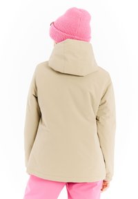 Beige geïsoleerde jas met een capuchon, gemaakt van textuurstof en met een minimalistisch ontwerp. G gedragen met felroze broeken en een roze gebreide muts.