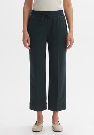 Femme portant un pantalon noir à jambes larges avec une taille élastique et un cordon, associé à des chaussures plates beiges et un haut blanc sans manches.