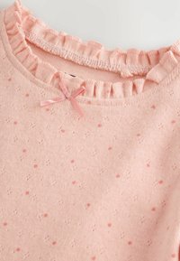 Weicher, pinkfarbener Strickstoff mit kleinen pinken Punkten, rüschengesäumtem Kragen und einem kleinen pinken Satinschleifchen in der Nähe des Ausschnitts.