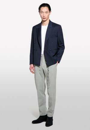 Blazer bleu marine à double boutonnage avec des revers nets, associé à un pantalon ajusté gris clair et des bottines noires. T-shirt à col rond blanc en dessous.