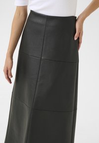 Falda de piel sintética negra con cintura alta, superficie texturizada, detalles en panel y forma ajustada que llega hasta los tobillos.
