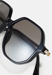 Ochelari de soare din plastic negru cu lentile gri în gradient, cadru pătrat și un accent auriu cu un detaliu rectangular transparent pe braț.