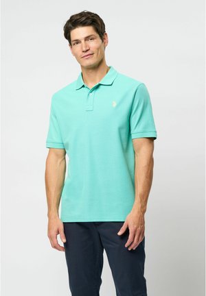 Svijetloplavi polo majica s kragnom, kratkim rukavima i suptilno teksturiranom tkaninom. Ima mali zlatni emblem na prsima.
