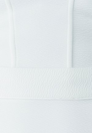 Valkoinen teksturoitu kangas, jossa on aaltoileva kuvio. Suunnittelussa on sileä vyöhyke alareunassa, mikä luo kerroksellista vaikutelmaa.