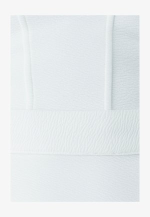 Tissu blanc texturé présentant un motif en vagues. Le design comprend une bande lisse en bas, créant un effet de superposition.