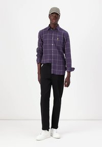 Purple checked button-up shirt, black trousers, and white sneakers. Also features a light gray cap with text. Short sleeves, relaxed fit.
