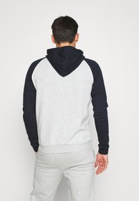 Grauer und marineblauer Raglan-Kapuzenpullover mit weicher Textur, gerippten Bündchen und Saum sowie einem Kängurutaschen-Design.