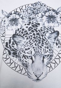 Camiseta de tela blanca con un diseño de estampado de leopardo en blanco y negro rodeado de elementos florales y acentos geométricos.
