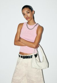 Rosa geripptes Tanktop mit besticktem Text, kombiniert mit einem schwarzen Gürtel mit silbernen Beschlägen und einer weißen Leder-Schultertasche.