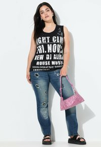Top nero senza maniche con testo bianco in grassetto, jeans blu strappati con dettagli sfrangiati, borsa a tracolla con strass rosa e sandali neri con platform.