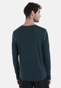 Langärmliges Hemd aus dunkelblauem Stoff mit weicher Textur, runder Ausschnitt und kontrastierendem hellblauen Saum entlang des Kragens und der Schultern.