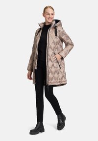 Pufferjas in lichtbeige met een ruitpatroon, ritssluiting aan de voorkant, capuchon, zijzakken en zwarte accenten, gecombineerd met zwarte broek en laarzen.