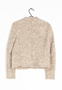 Beige uldblandingsjakke, struktureret finish, cropped design, synlige sømme og rund krave. Hængende på en sort krog mod en hvid baggrund.