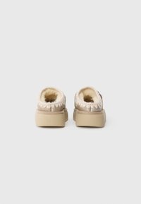 Beige slip-on sko med en myk, pelsforet innside, sømdetaljer rundt kragen og en tykk, solid såle.